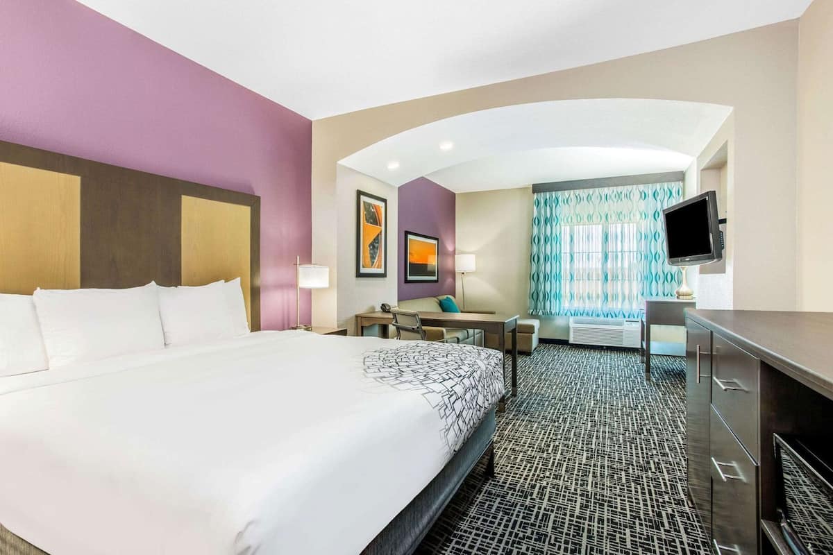 Habitación de hotel con una cama grande, un escritorio, una silla, un televisor y una ventana con cortinas estampadas.