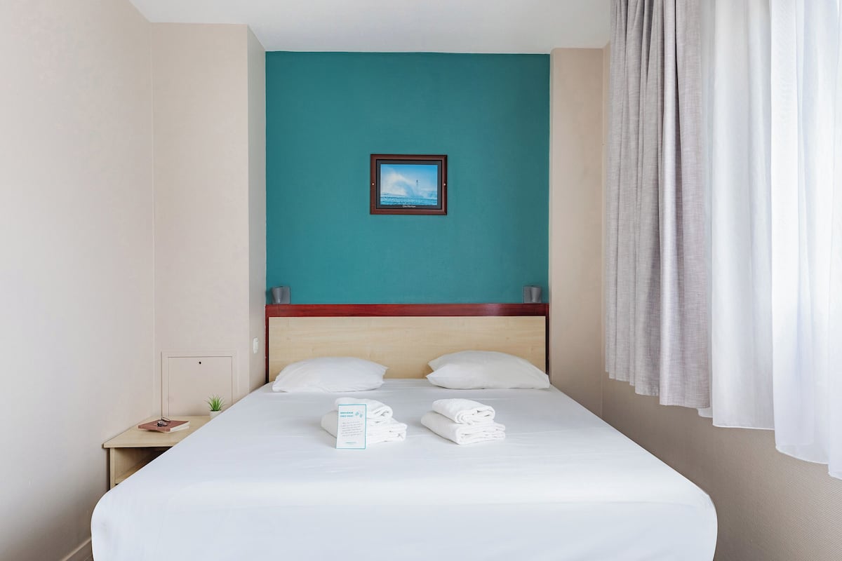 A hotel room with a bed, a nightstand, a small plant, and a framed picture on the wall.