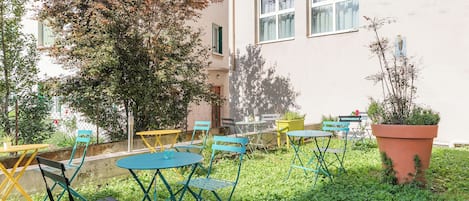 An outdoor seating area with tables and chairs, a potted plant, and a building in the background.
