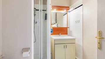 Une salle de bain avec une douche à parois de verre, un lavabo avec un miroir au-dessus et des toilettes.