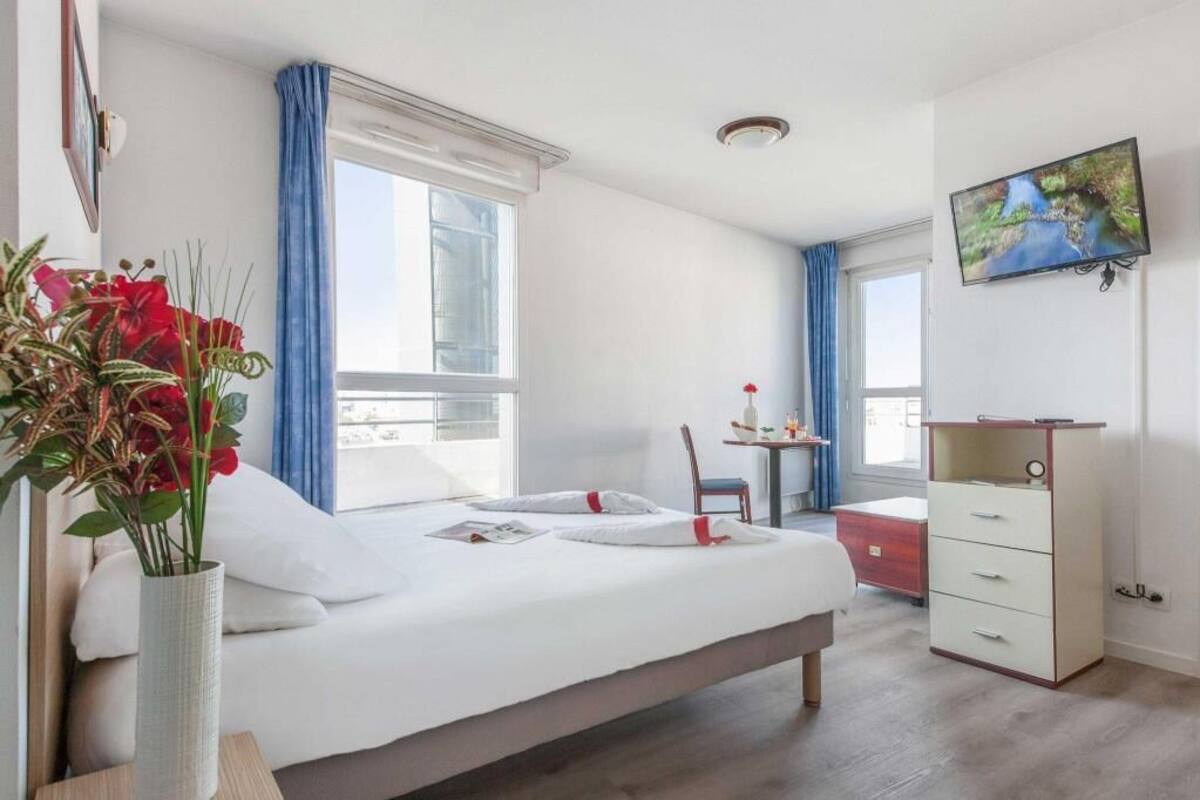 A hotel room with a bed, a desk, a chair, a TV, and a window with curtains.