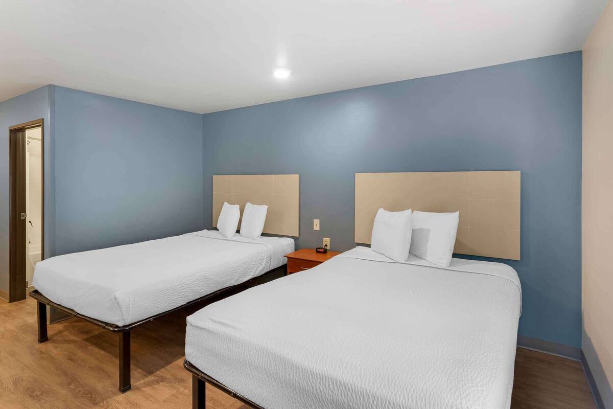 A hotel room with two single beds, wooden flooring, and light blue walls.