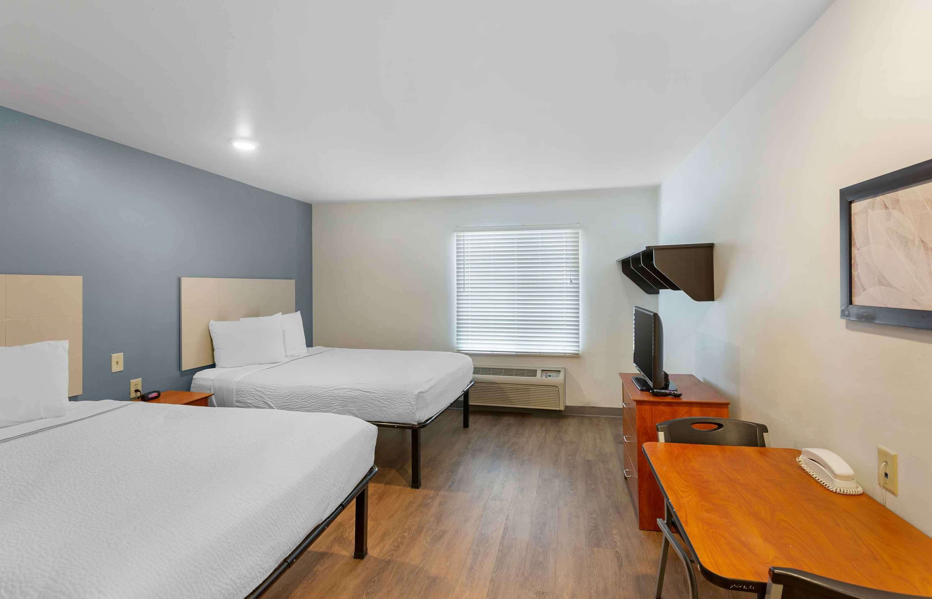 Habitación de hotel con dos camas, un escritorio, una silla, televisión y ventana con persianas.