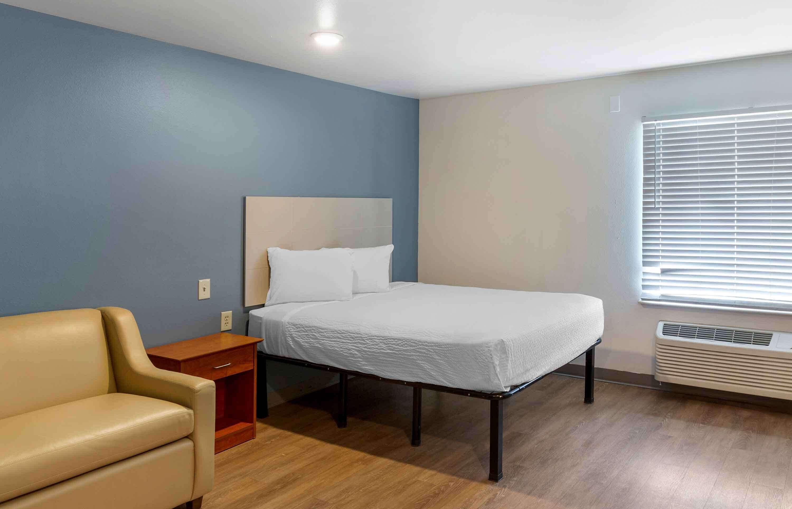A room with a bed, a nightstand, a chair, and a window with blinds.