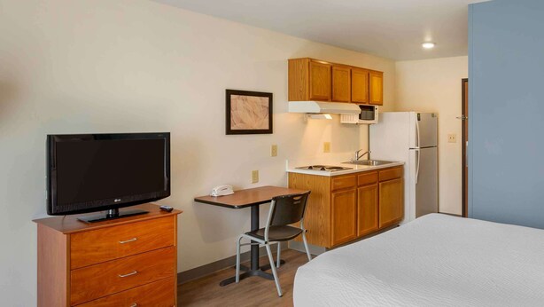 Een compacte hotelkamer met een bed, een televisie op een houten dressoir, een kleine kitchenette met een magnetron en een stoel.