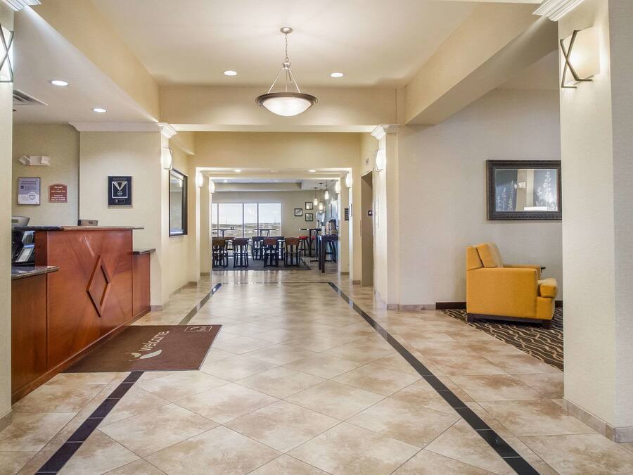 Un hall de hotel con mostrador de recepción, un sillón amarillo y vistas al comedor.