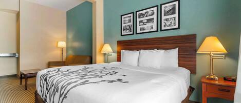 Habitación de hotel con una cama grande, dos mesitas de noche con lámparas, una silla y una pared decorada con cuadros.