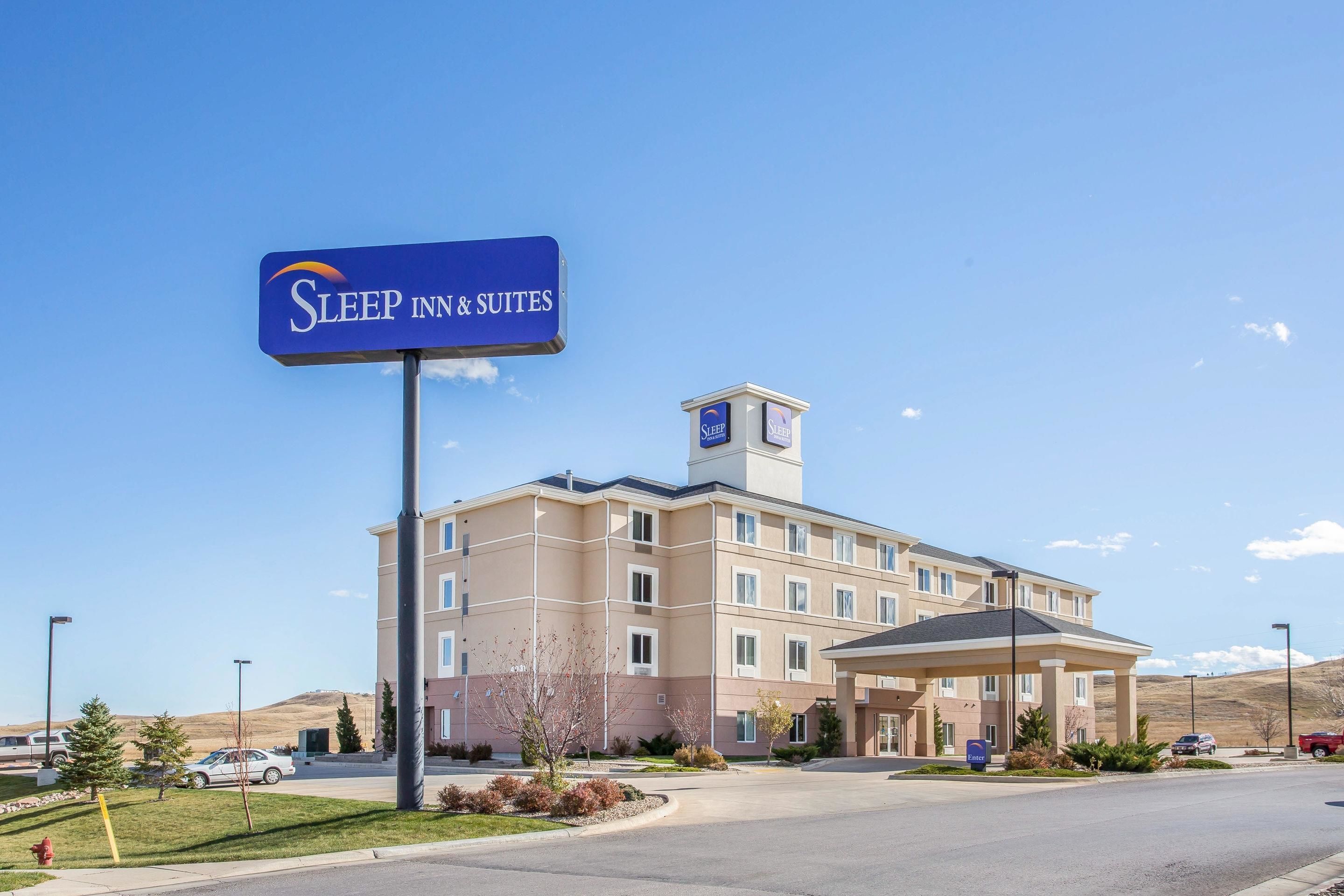 Een Sleep Inn & Suites hotel met een heldere lucht, een parkeerplaats en een verzorgd gazon.