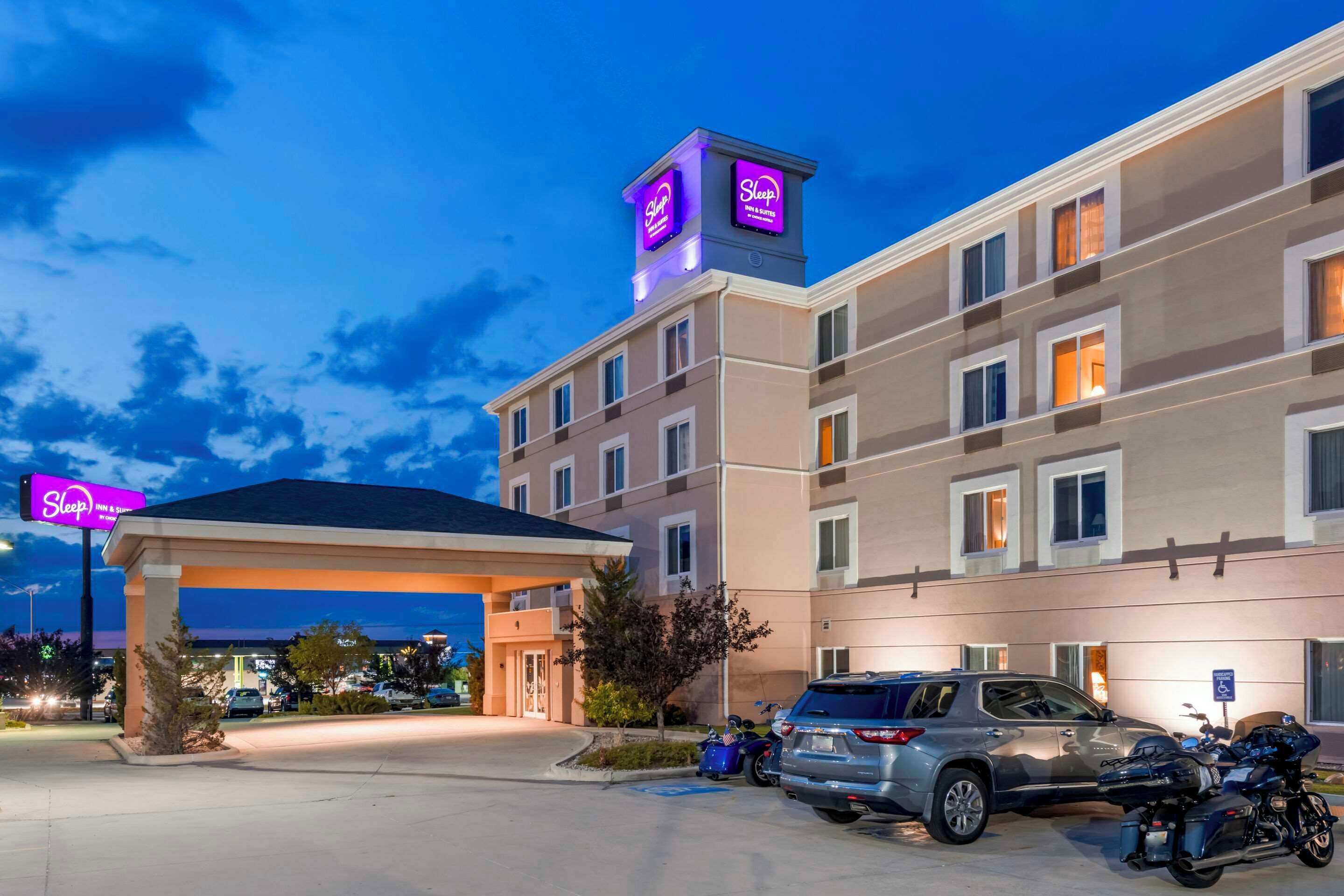 A hotel with a covered entrance, multiple floors, and a parking area with cars and motorcycles.