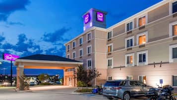 Un hotel con entrada cubierta, varios pisos y un estacionamiento con coches y motocicletas.