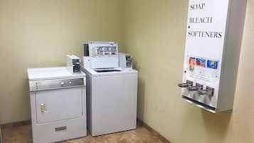 Uma área de lavanderia com máquina de lavar, secadora e dispensador de amaciante para sabão e água sanitária.