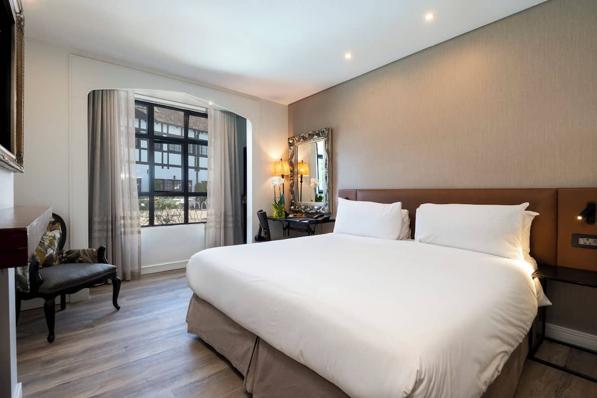 A hotel room with a large bed, a desk, a chair, a mirror, and a window with curtains.