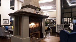 A modern living room with a stone fireplace, a sofa, and a blue armchair. - ANEW Hotel Hilton Pietermaritzburg (Hilton)