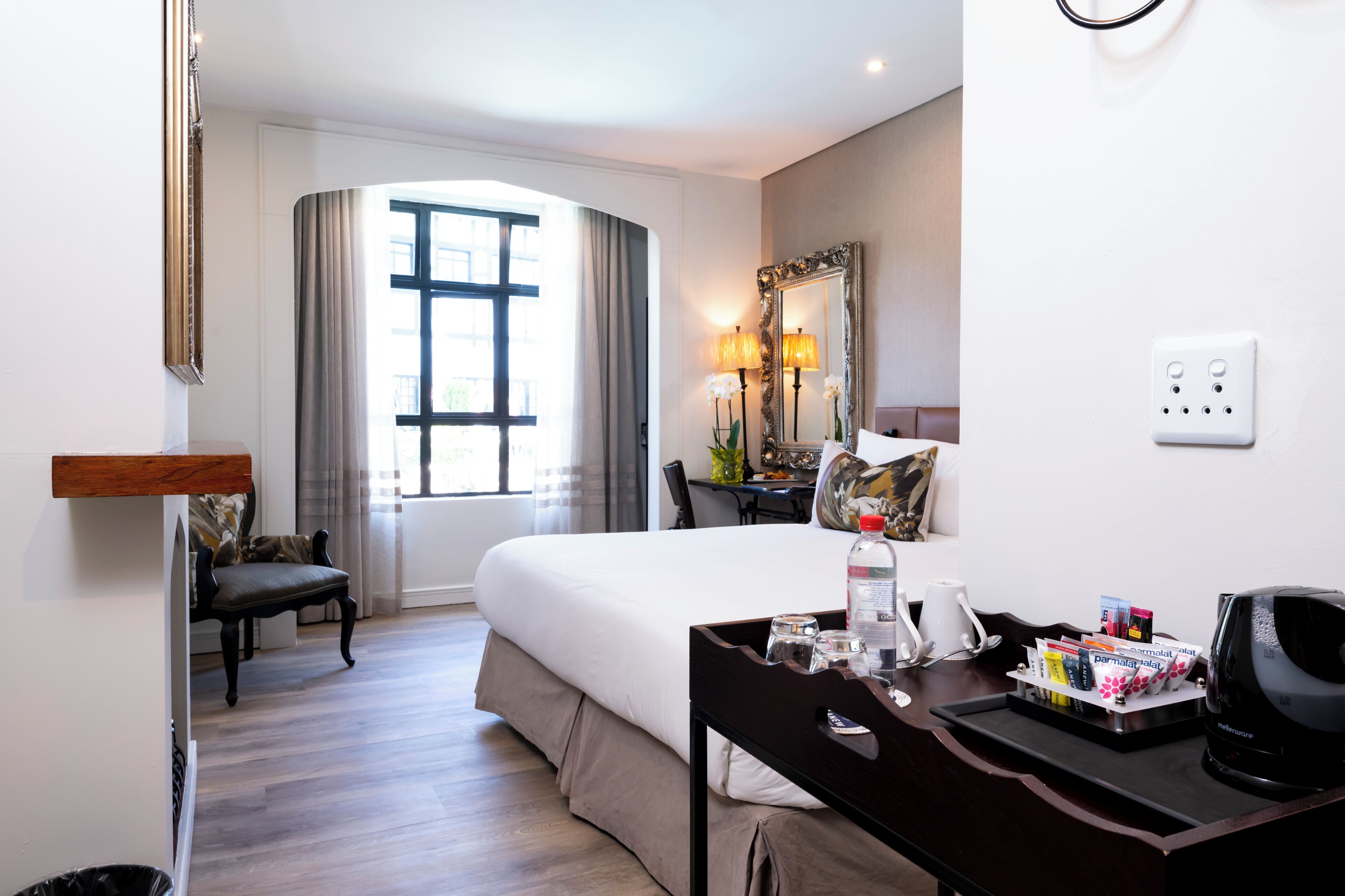 A hotel room with a bed, a desk with a coffee maker, a lamp, and a window with curtains.