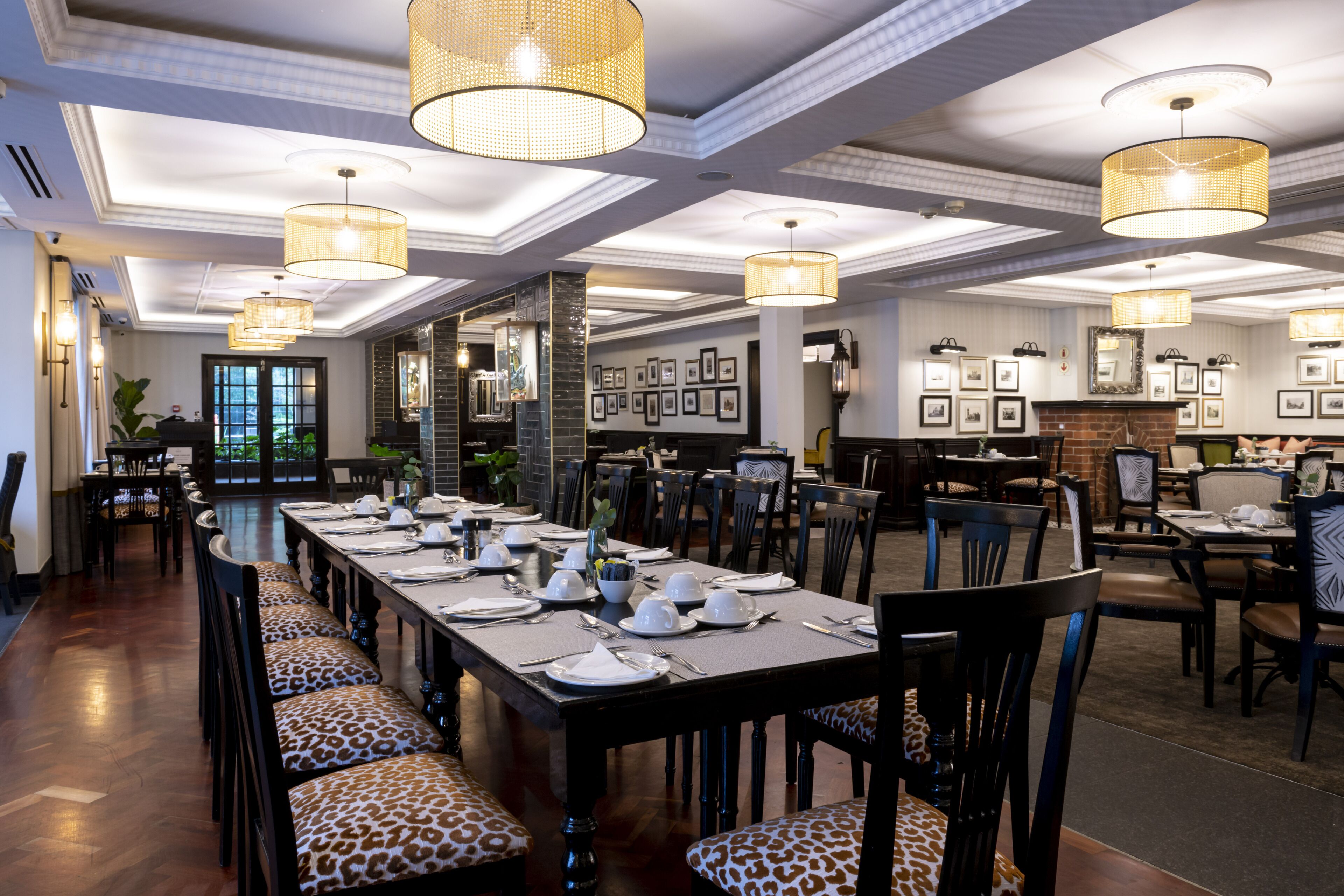 A long dining table set with chairs, large hanging lamps, and framed pictures on the walls.