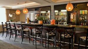 A bar area with a long counter, multiple chairs, and hanging pendant lights. - ANEW Hotel Hilton Pietermaritzburg (Hilton)