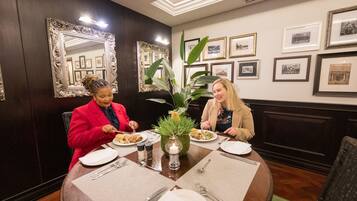 Twee personen dineren aan een tafel, met lijstjes op de muur.