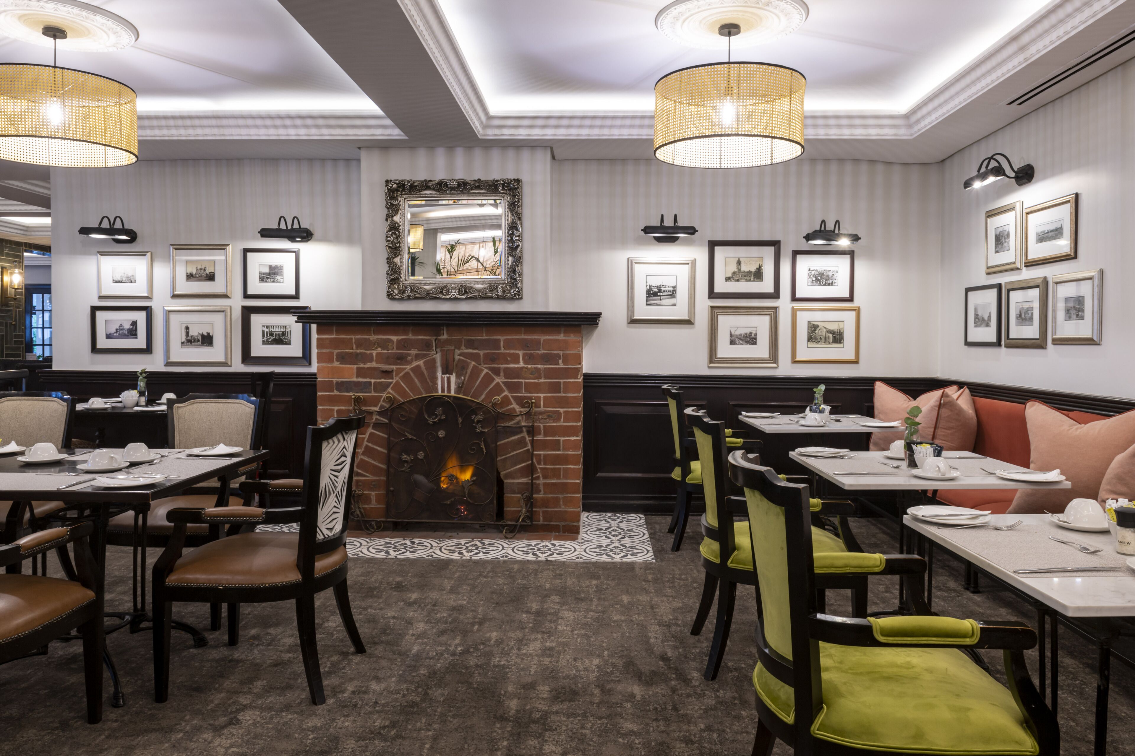 A dining area with a brick fireplace, framed pictures on the walls, and tables set for dining.