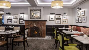 A dining area with a brick fireplace, framed pictures on the walls, and tables set for dining.
