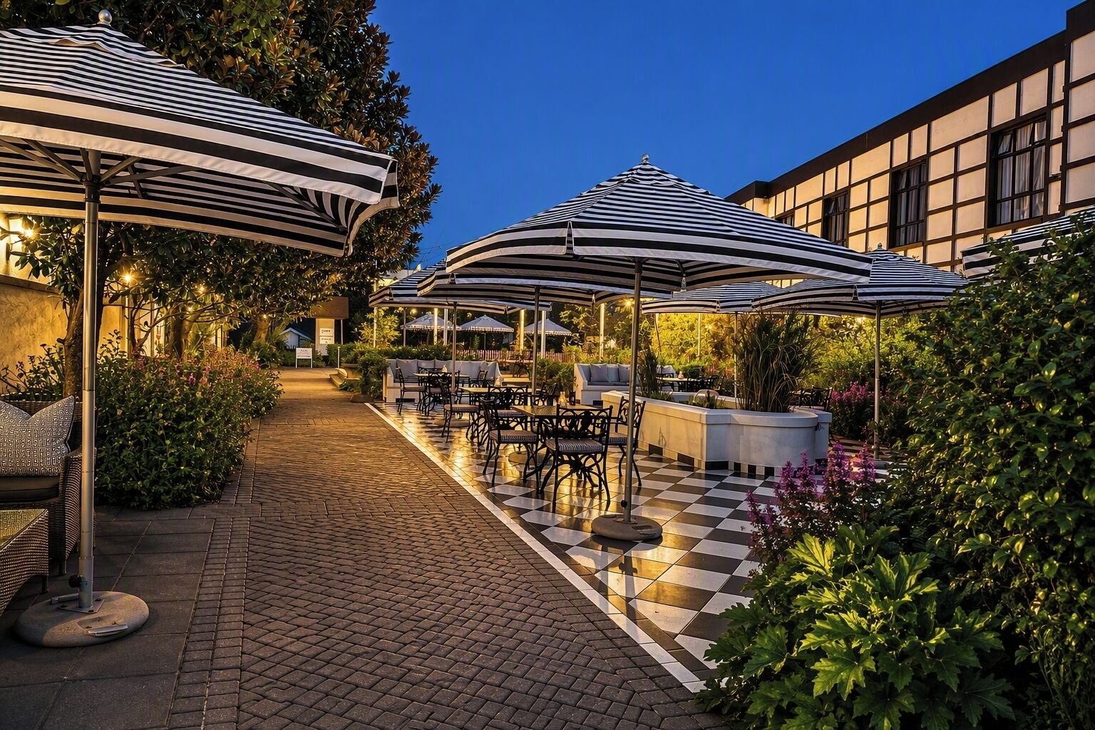 Un patio al aire libre con piso a cuadros, sombrillas a rayas y mobiliario exterior.