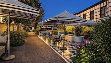 Un patio al aire libre con piso a cuadros, sombrillas a rayas y mobiliario exterior.