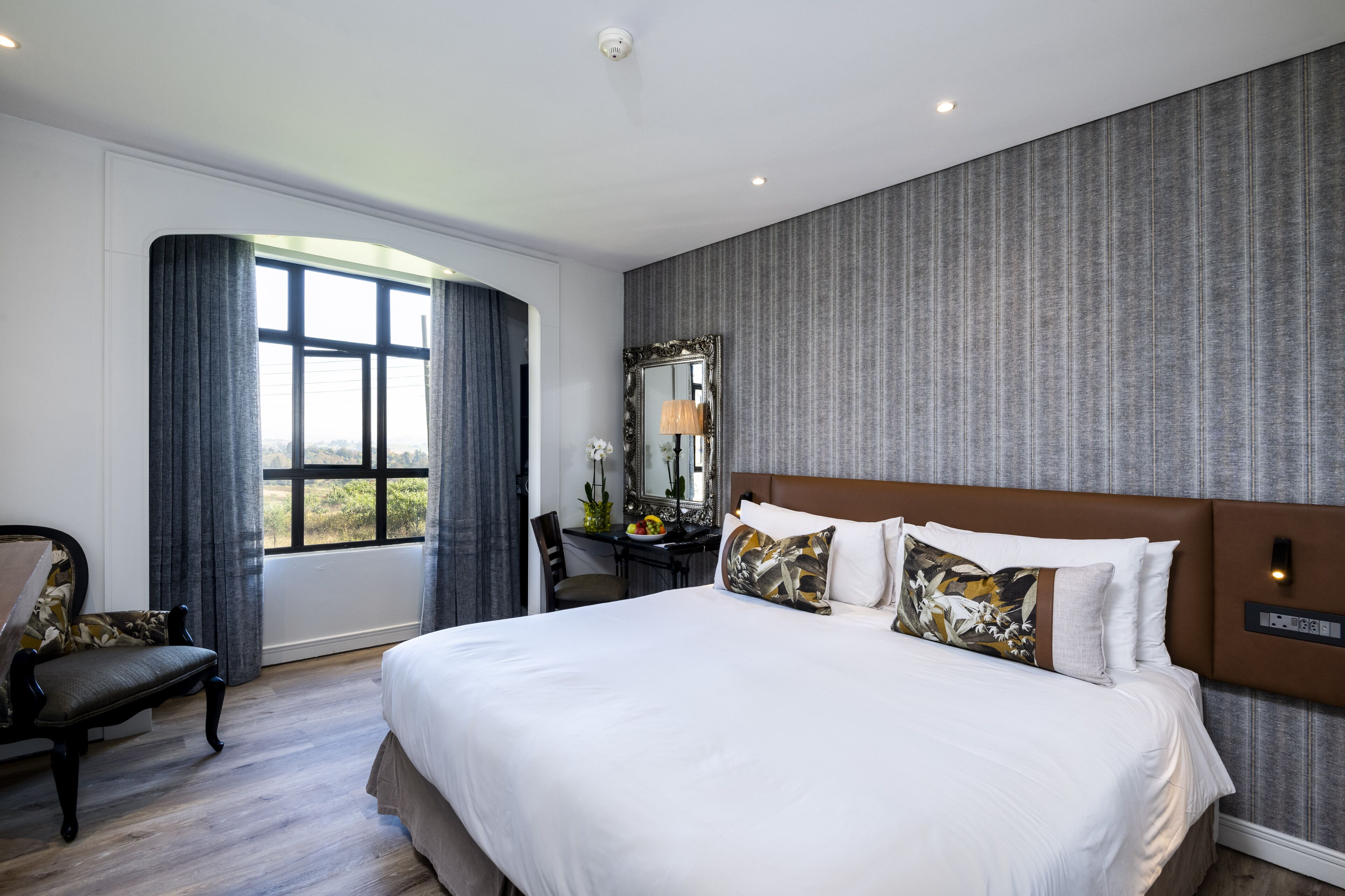A hotel room with a large bed, a desk, a chair, a mirror, and a window with curtains.