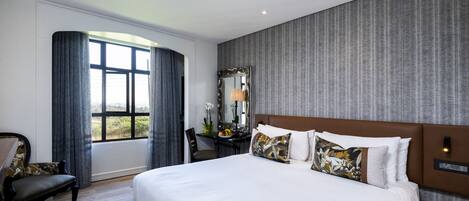 A hotel room with a large bed, a desk, a chair, a mirror, and a window with curtains.