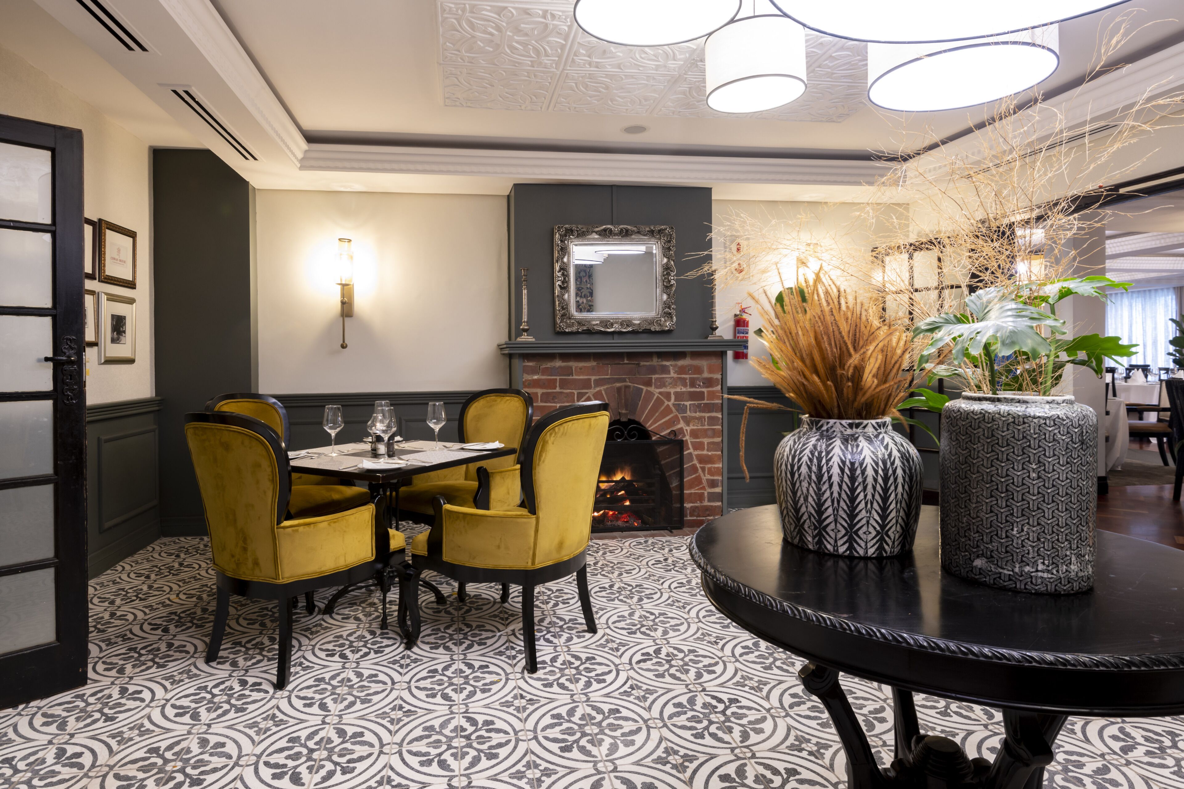 A dining area with a brick fireplace, yellow chairs, and patterned floor tiles.