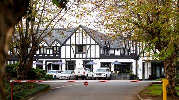 A traditional black-and-white building with a prominent entrance, a gated driveway, and parked cars.