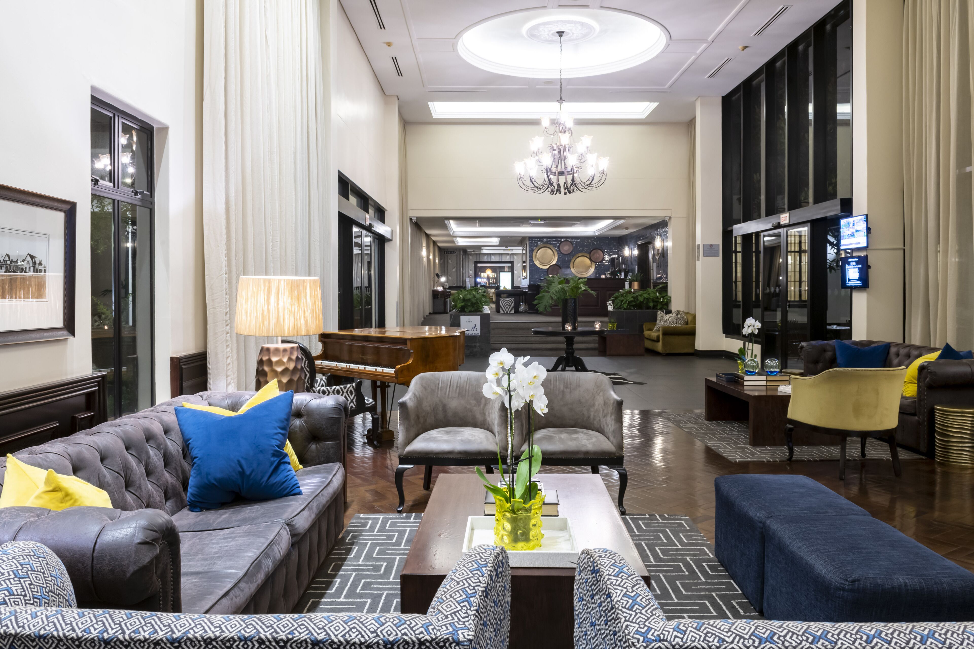 A spacious lobby with a grand chandelier, leather sofas, and a central coffee table with a vase of flowers.