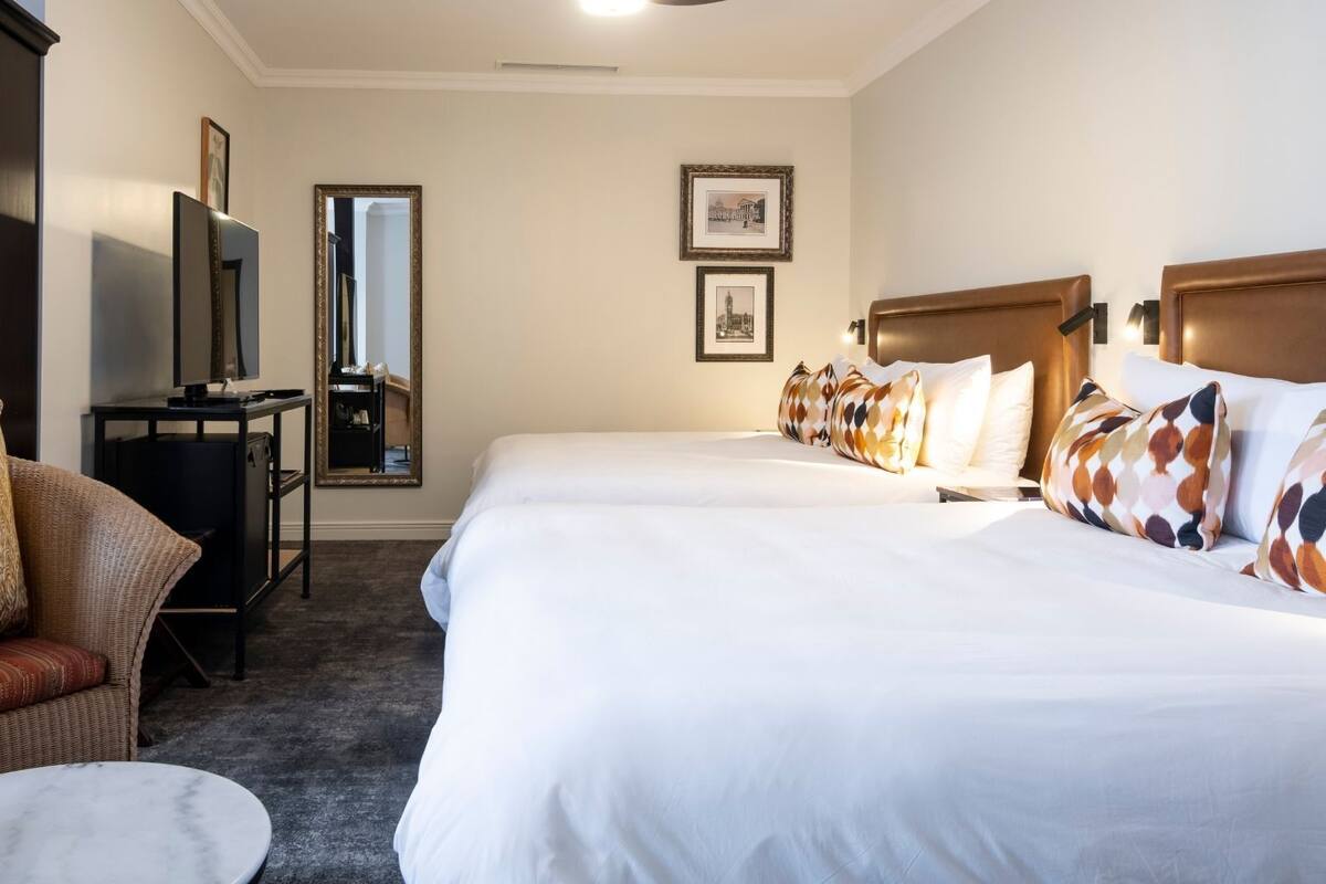 A hotel room with two beds, a desk, a chair, and a large mirror.