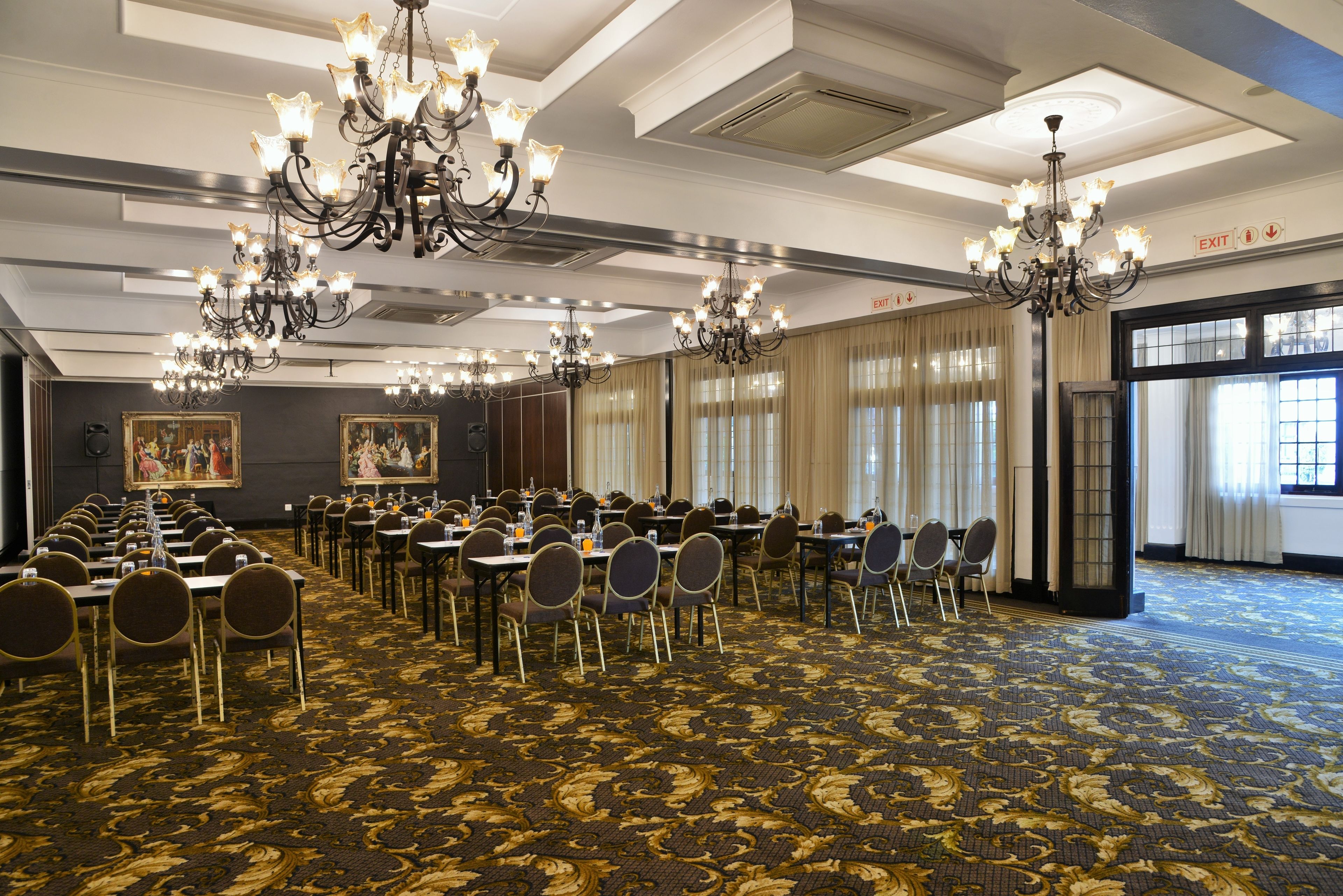 A conference room with multiple tables and chairs, chandeliers, and large windows with curtains.