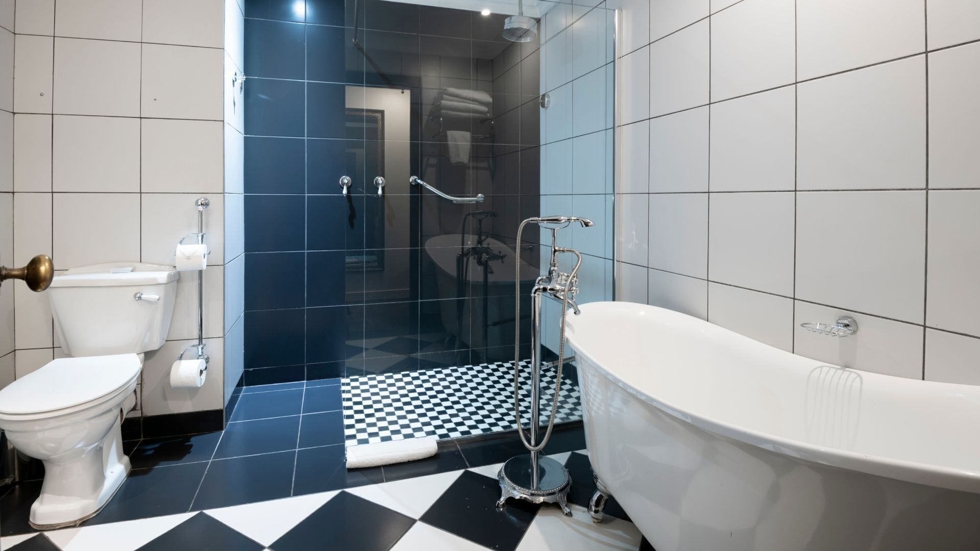 Une salle de bain avec des toilettes blanches, une baignoire et un espace douche doté d’un carrelage à motifs géométriques.