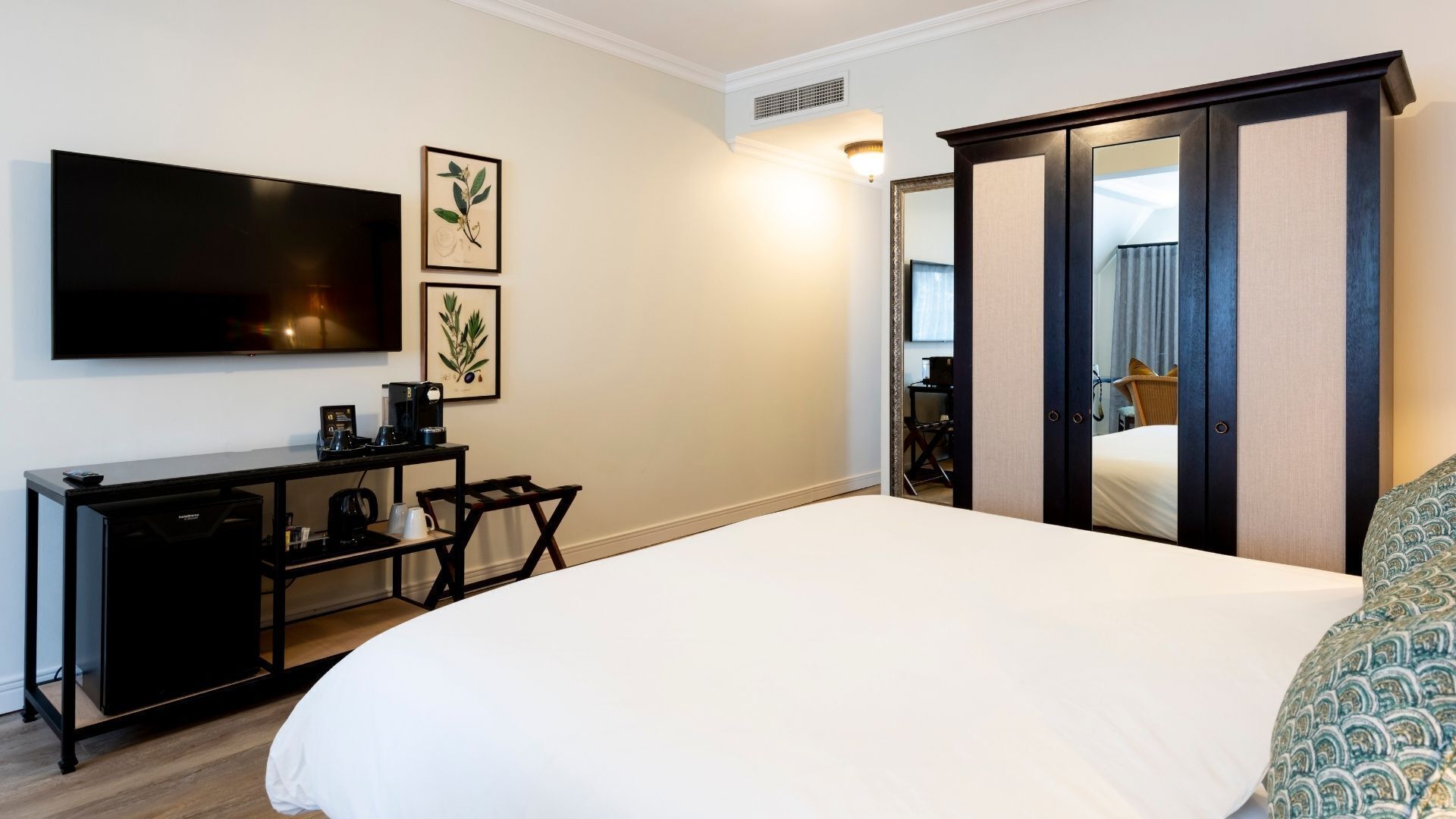Una habitación de hotel con una cama grande, un televisor de pantalla plana en la pared, un escritorio con cafetera y un armario con espejo.