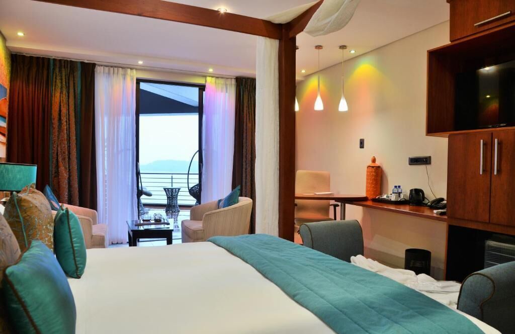 Habitación de hotel con una cama, dos sillones, un escritorio con televisor y vistas al mar.