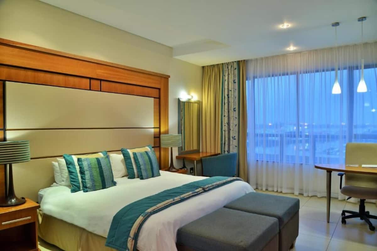 A hotel room with a large bed, a desk, a chair, and a view of the city.