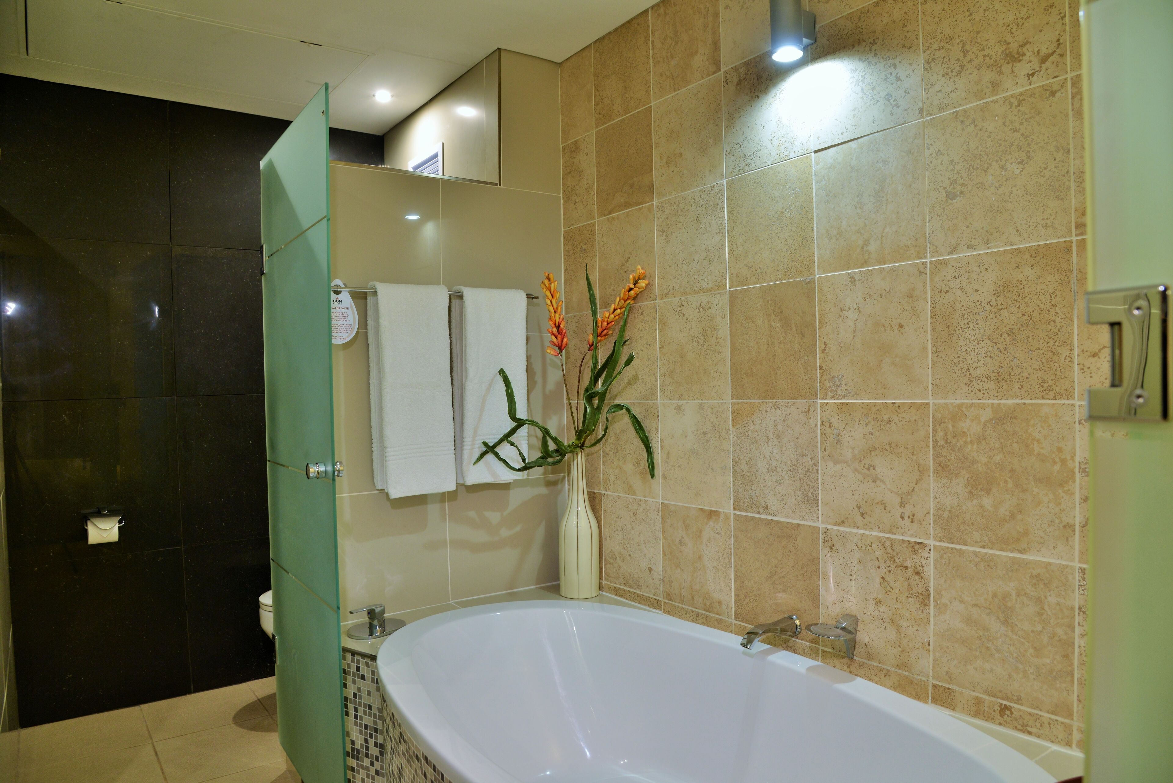 A bathroom with a bathtub, a toilet, a shower area, and a vase with flowers.