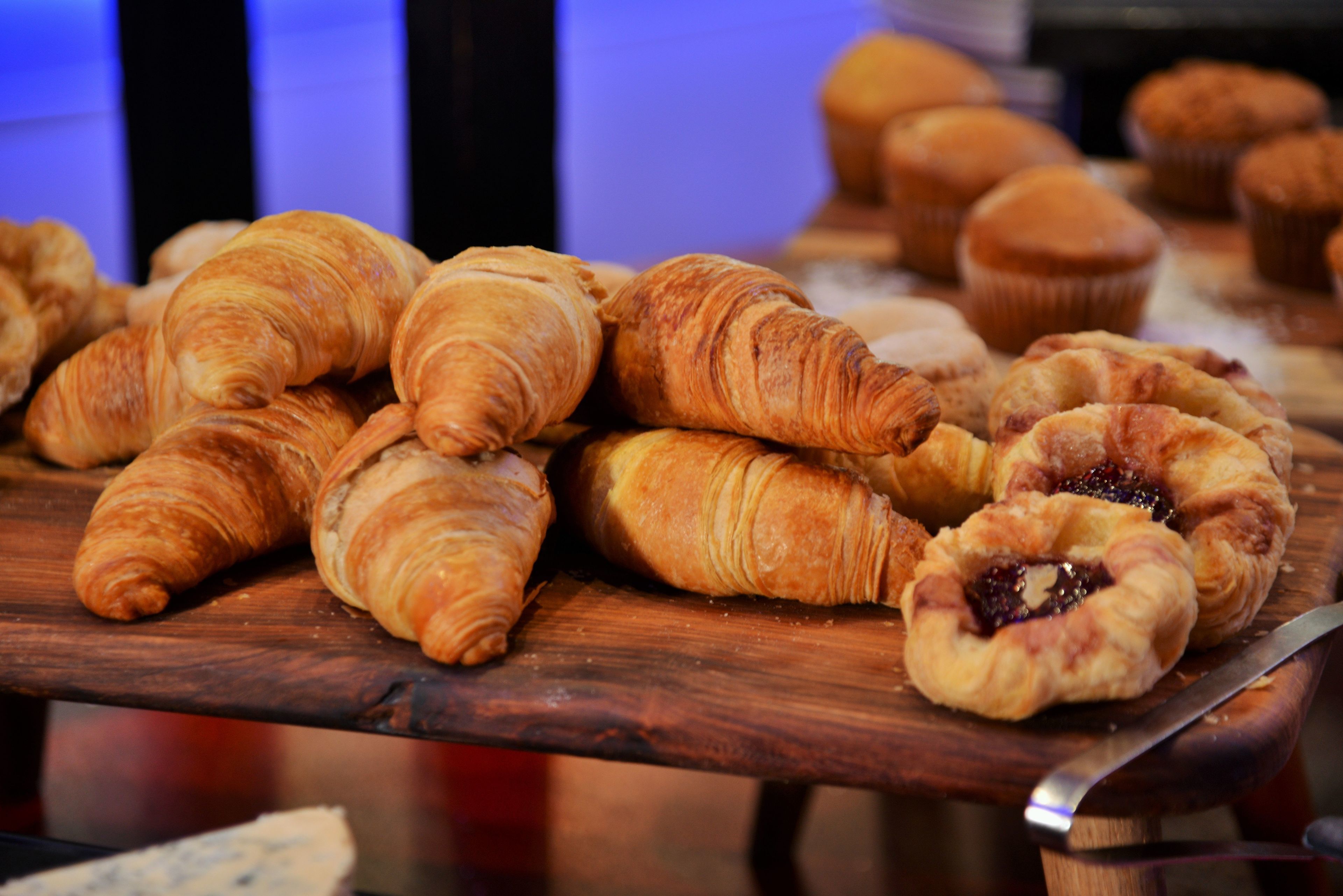 A wooden table with various pastries, including croissants and muffins.