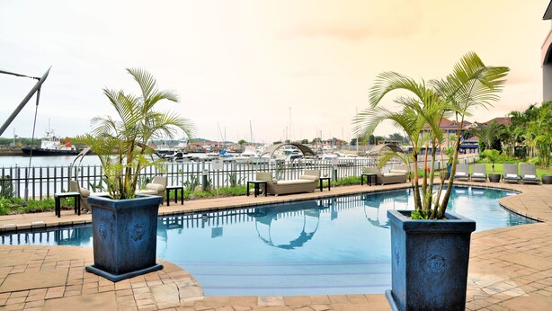 A swimming pool with lounge chairs and potted plants, overlooking a marina with boats. - BON Hotel Waterfront Richards Bay (Richards Bay)