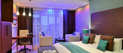 A hotel room with a large bed, two armchairs, a desk, and a window with curtains.