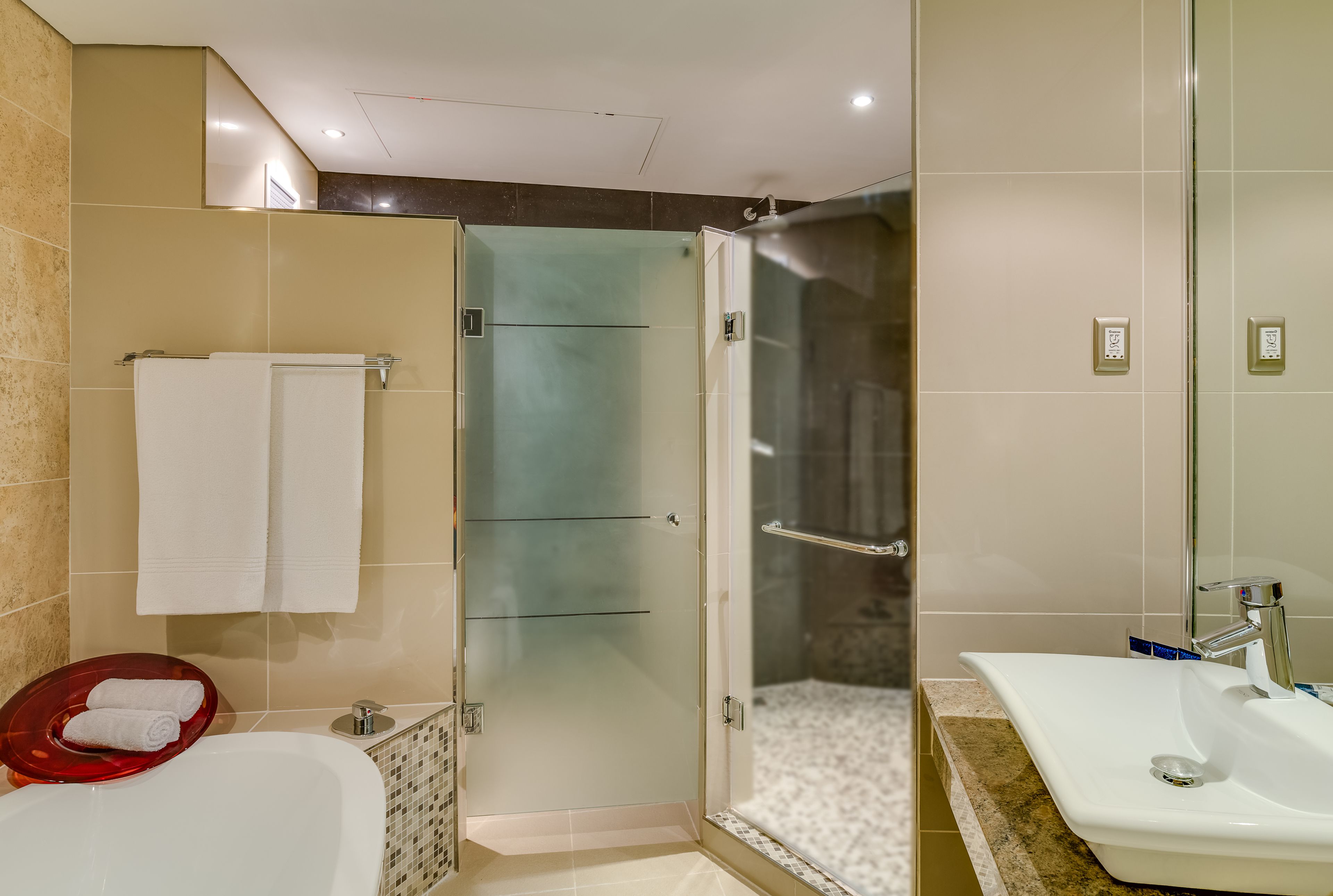 A modern bathroom with a glass-enclosed shower, a white sink, and a red bath mat.