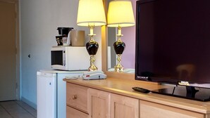 A hotel room with a wooden dresser, a television, a microwave, and two lamps. - Travel Inn (Hearst)