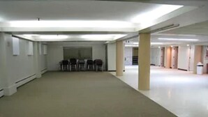 A large, empty room with a high ceiling, carpeted floor, and several columns. - Travel Inn (Hearst)