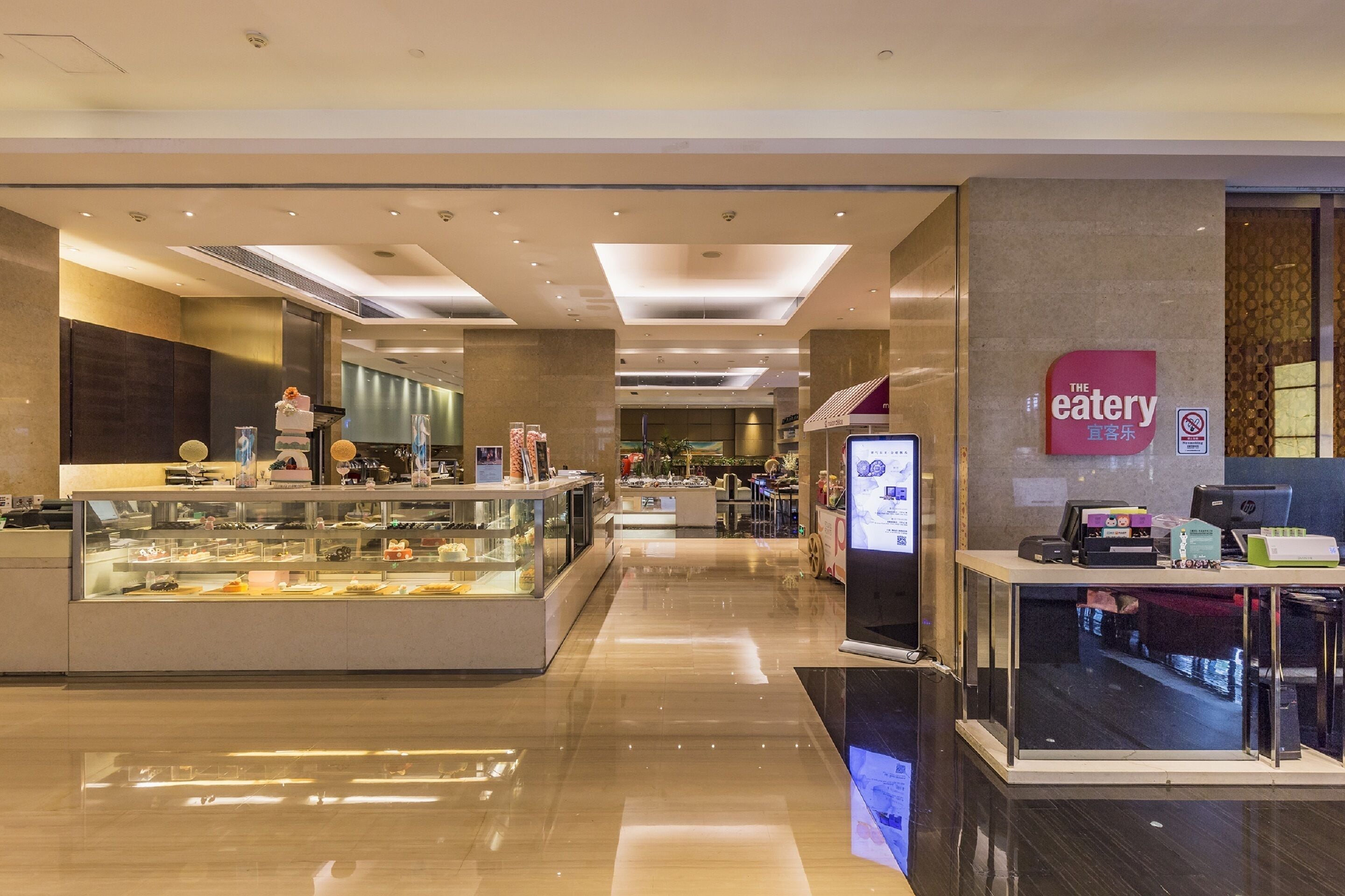 A modern restaurant with a glass display case filled with desserts, a digital menu board, and a clean, polished floor.