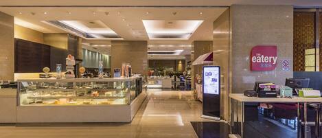 A modern restaurant with a glass display case filled with desserts, a digital menu board, and a clean, polished floor.