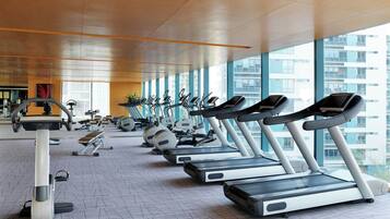 Un gimnasio con cintas de correr alineadas, bicicletas estáticas y diverso equipamiento de fitness.