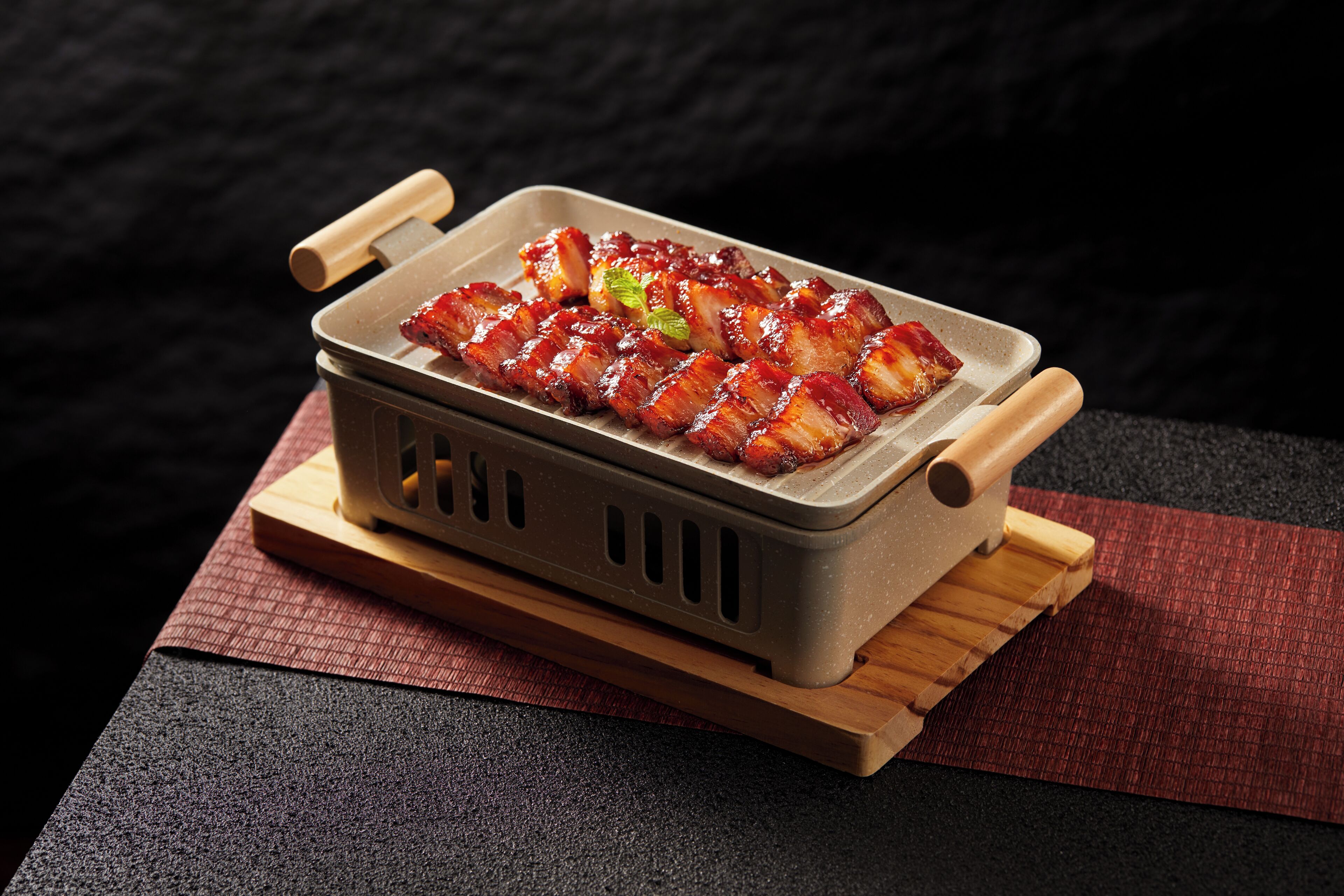 Una parrilla rectangular con asas a los lados, que contiene varios alimentos, colocada sobre una tabla de madera.