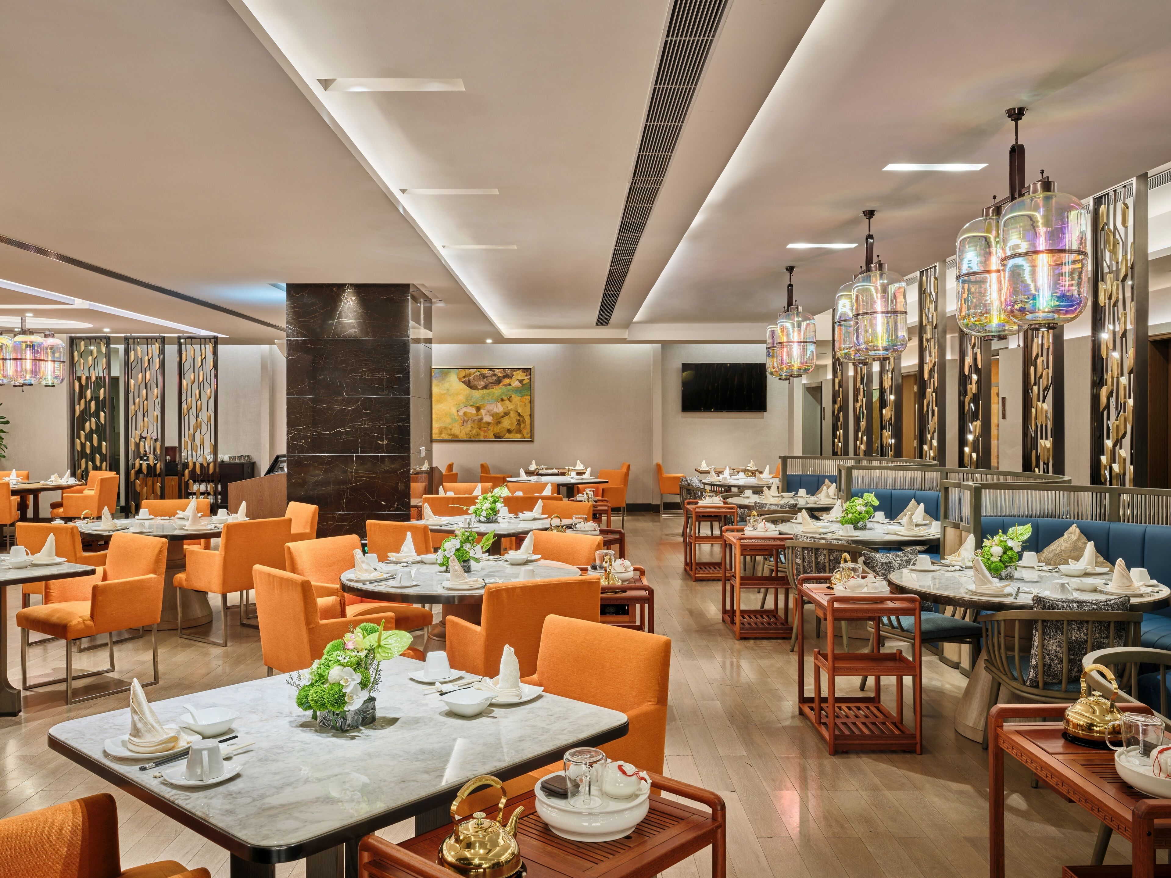 A modern restaurant with multiple dining areas, each featuring round tables and orange chairs.