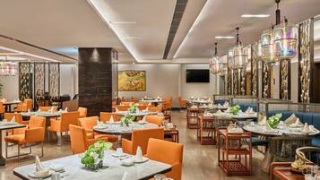 A modern restaurant with multiple dining areas, each featuring round tables and orange chairs.
