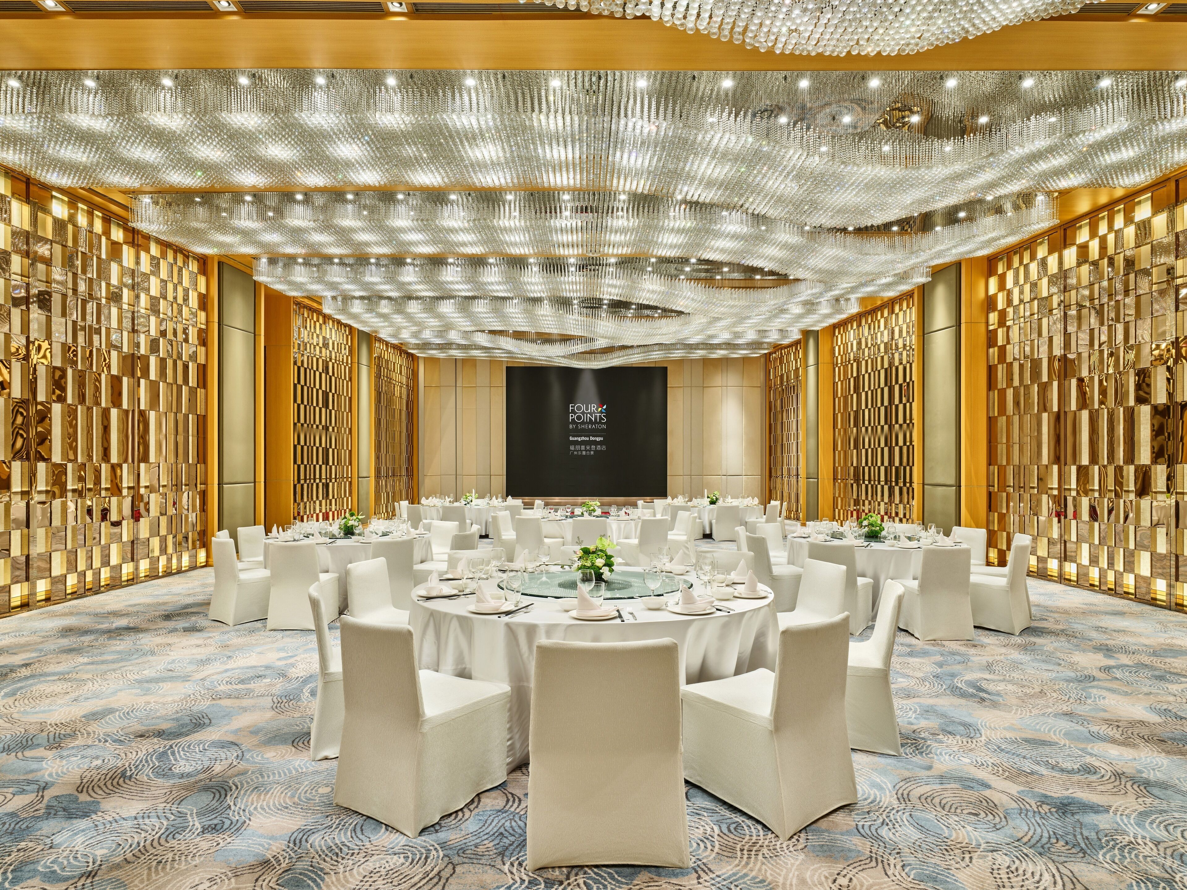 A conference room with round tables, white chairs, and a large screen in the center.